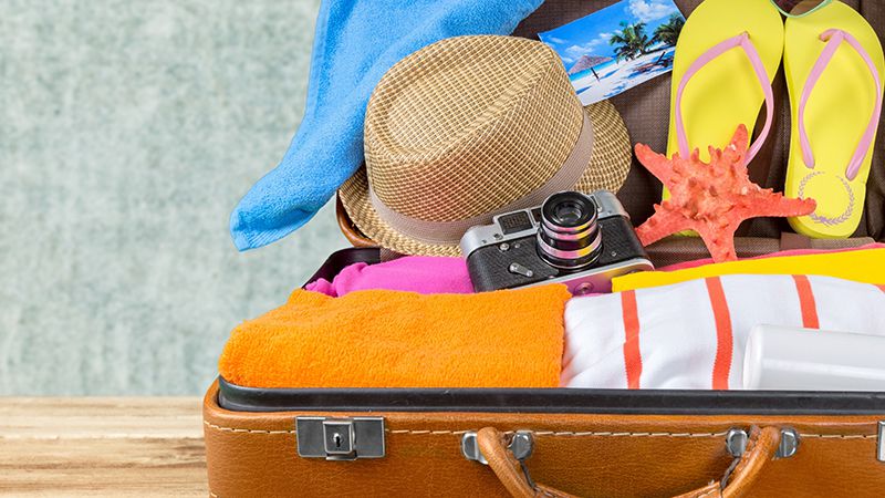 resväska med reseprylar som solhatt, flipflops, kamera och vykort
